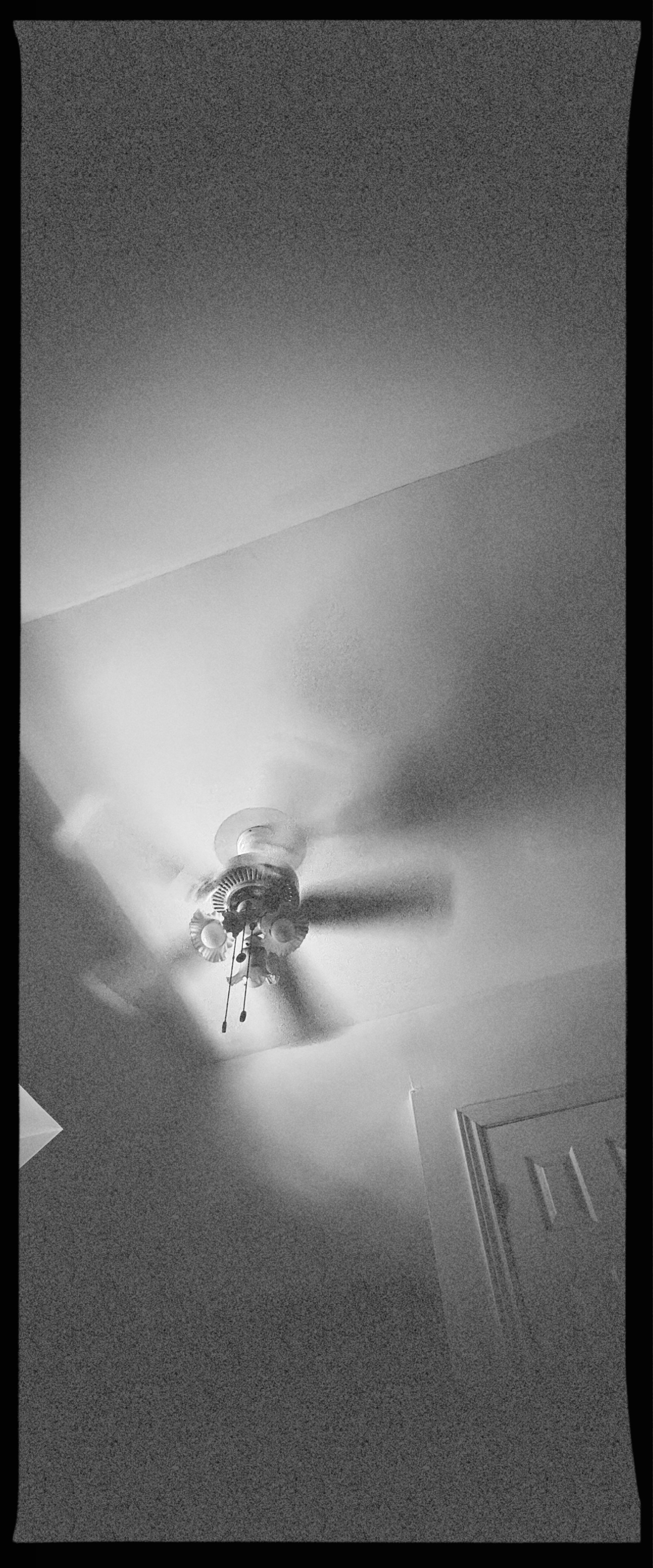 Tall black and white panoramic frame of a spinning ceiling fan